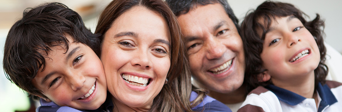 Happy family of four smiling together in close portrait pose indoors.
